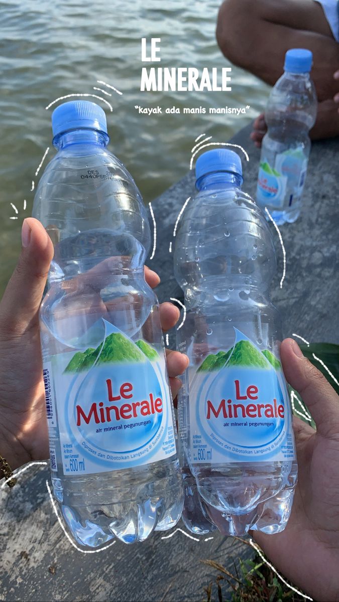 two bottles of mineral water being held by someone's hands in front of the water