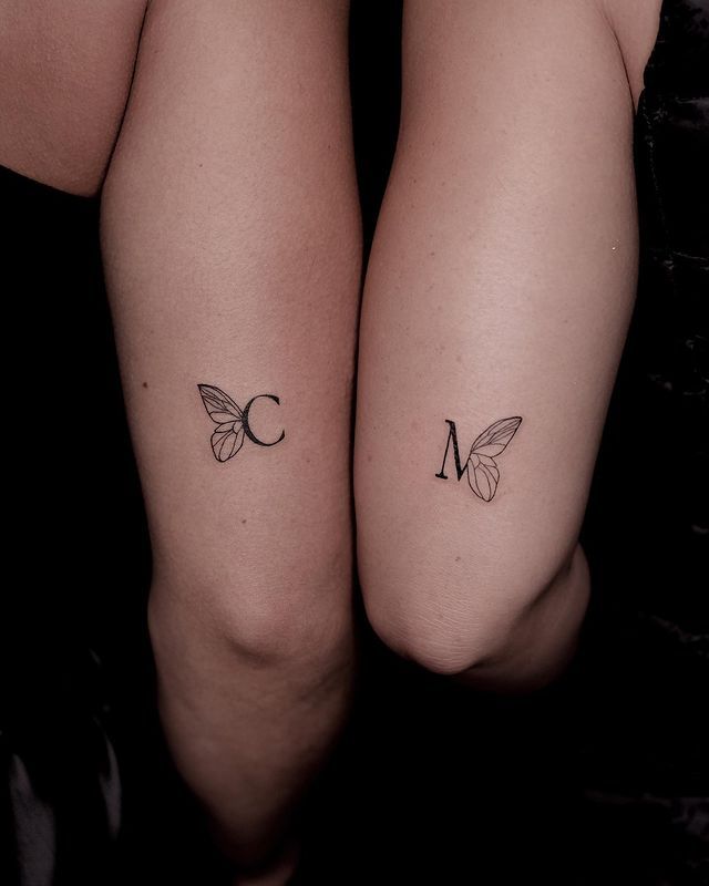 two women with matching tattoos on their legs, both showing the letter m and butterfly