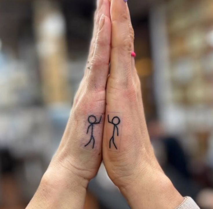 two people holding hands with small tattoos on their palms, one has a stick man and the other is a woman's hand