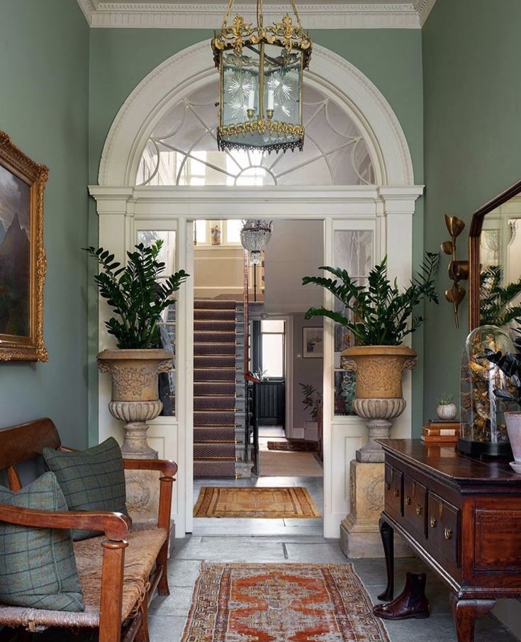 an entry way with green walls and white trim, wooden furniture and potted plants