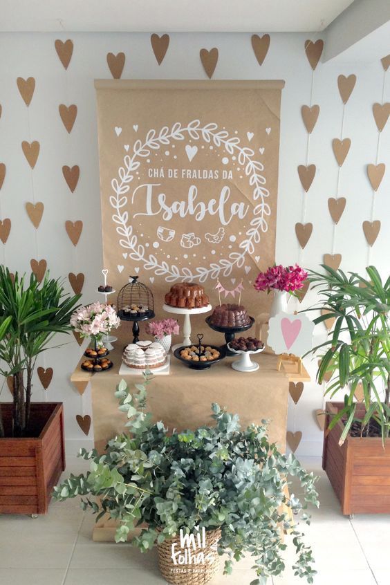 a table topped with cakes and plants next to a wall covered in heart shaped stencils