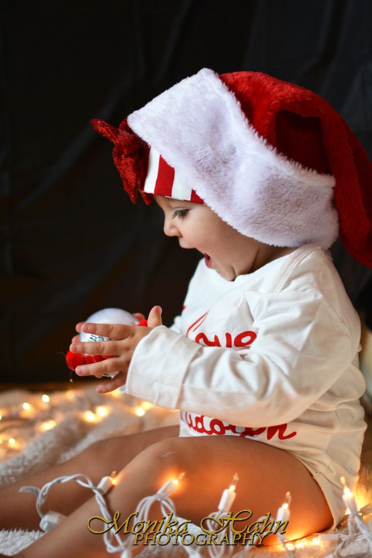 a small child wearing a santa hat and holding a christmas ornament while sitting on a bed