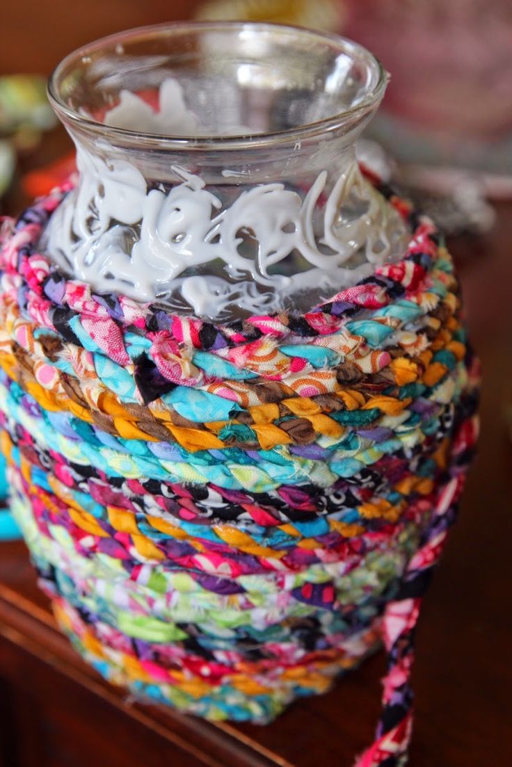 a glass vase sitting on top of a wooden table covered in multicolored fabric