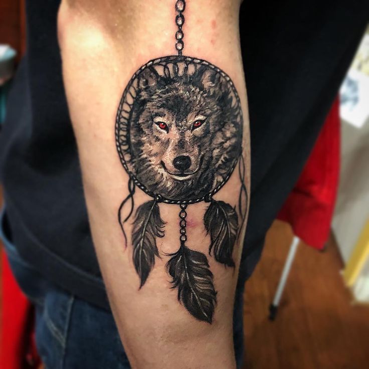 a man with a tattoo on his arm has a wolf dream catcher in it's hand