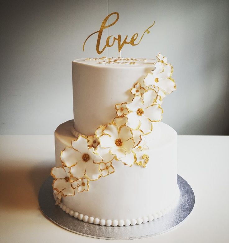 a white wedding cake with gold flowers and the word love written on top is sitting on a table