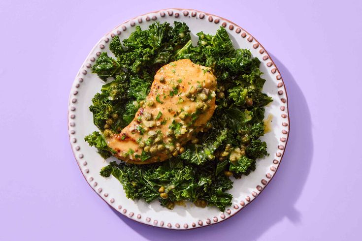 a white plate topped with meat and greens on top of a purple tablecloth next to a fork