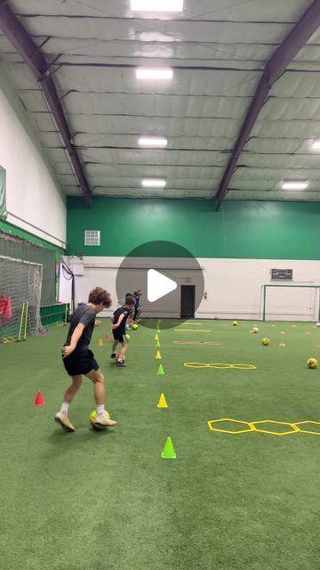 children playing soccer in an indoor facility with green walls and yellow cones on the floor