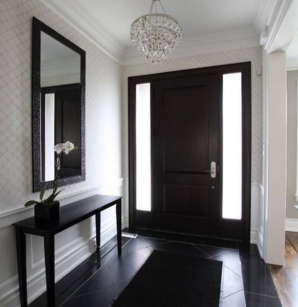 a hallway with a black door, mirror and table in front of the entranceway