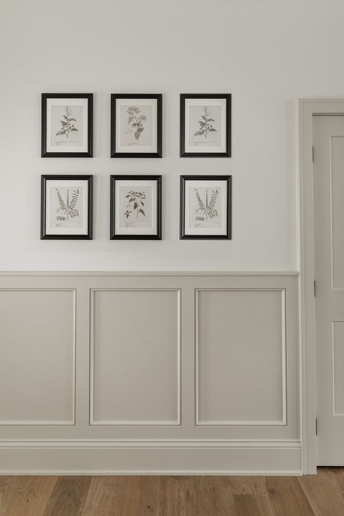 four framed pictures hang on the wall above a wooden floor in a room with white walls and wood floors