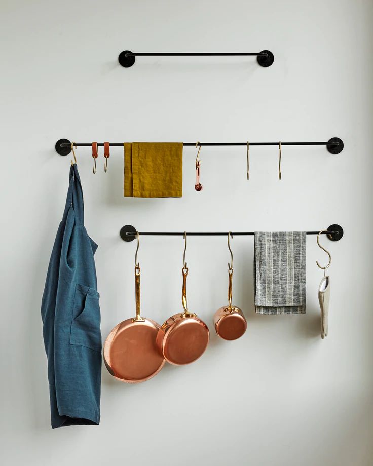 pots and pans are hanging on the wall next to an iron rack with hooks