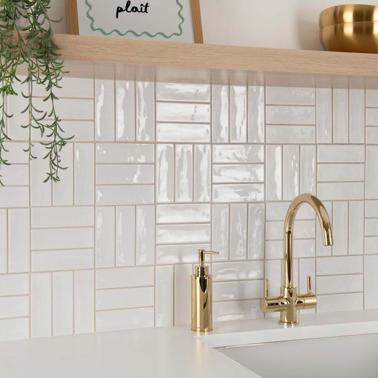 a kitchen with white tile and gold faucets on the counter top, next to a potted plant