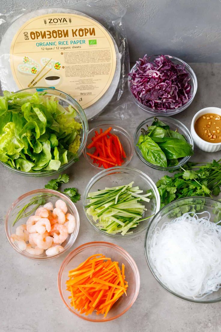 bowls filled with different types of vegetables and sauces on top of a gray surface