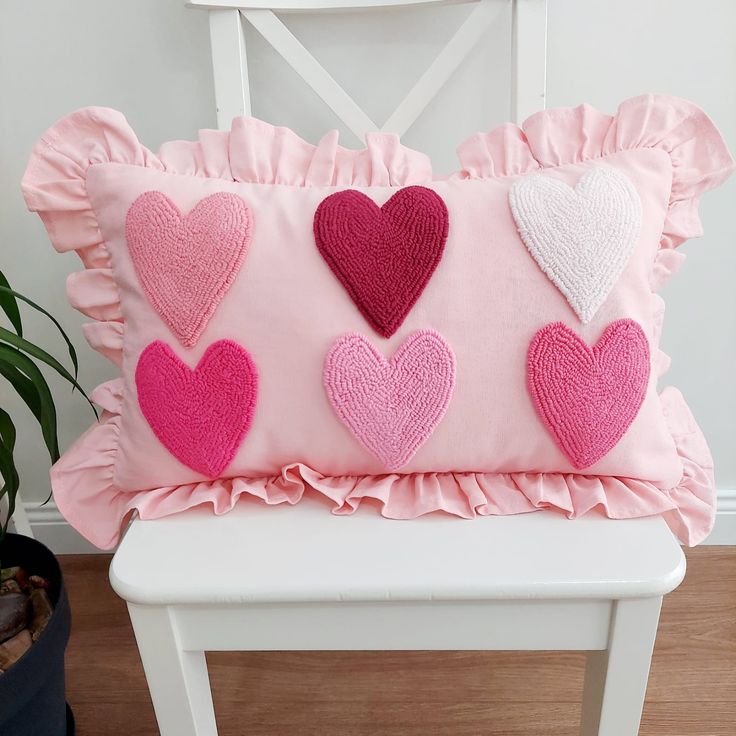 a pink pillow with hearts on it sitting on a white chair next to a potted plant