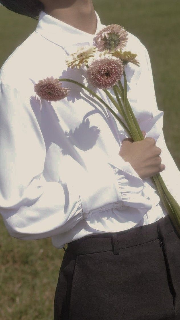 a woman holding flowers in her hands while wearing a white shirt and black pants,