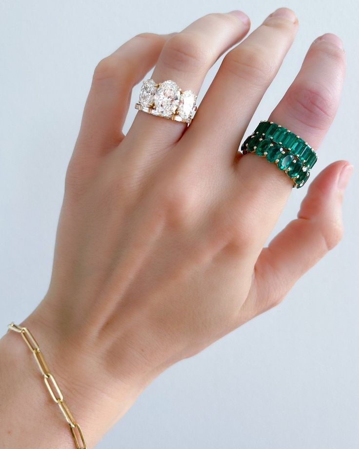 a woman's hand with two rings on it and an emerald ring in the middle