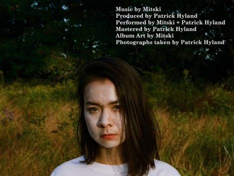 a woman with white paint on her face standing in tall grass