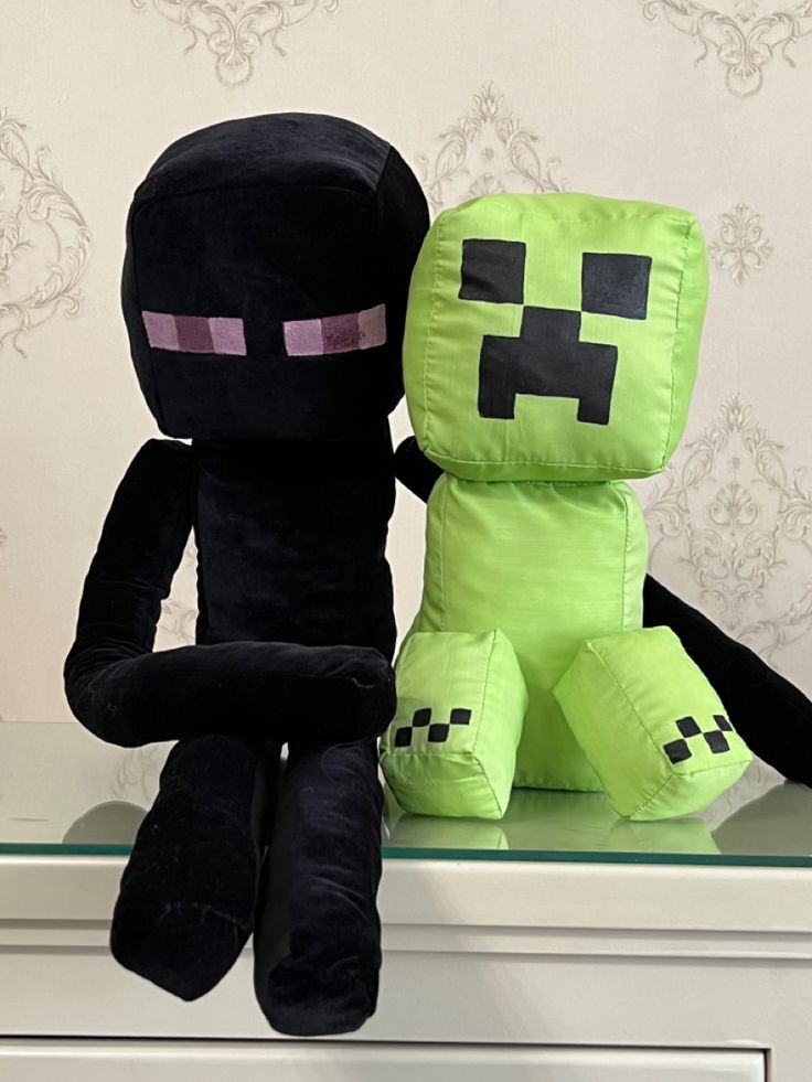 two black and green minecraft stuffed animals sitting on top of a white dresser next to each other