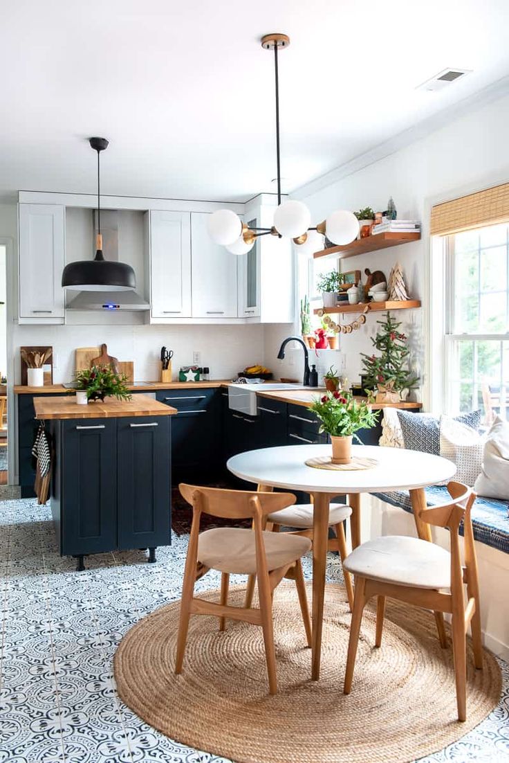 a woman standing in a kitchen next to a table with chairs and potted plants on it