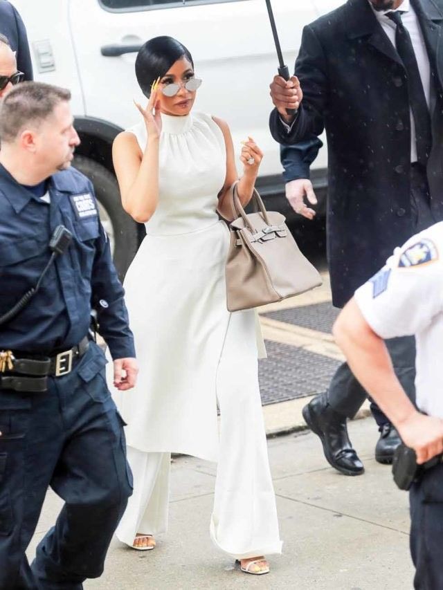 a woman in a white dress holding an umbrella while walking down the street with police behind her