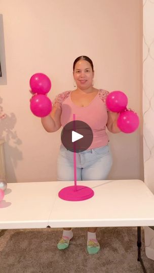 a woman is holding pink balloons in front of her face while standing at a table