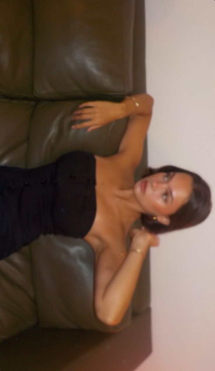 a woman in black shirt laying on top of a brown couch next to a wall