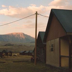 an old barn sits in the middle of a grassy field with mountains in the background