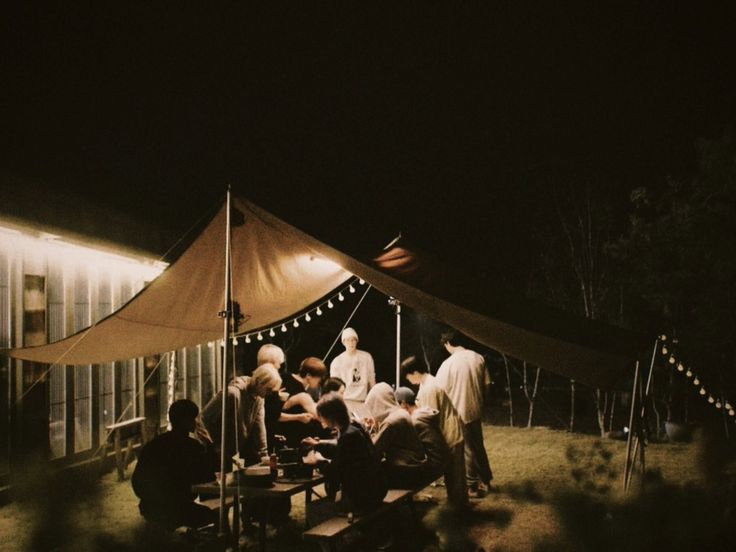 a group of people sitting around a table under a tent in the grass at night