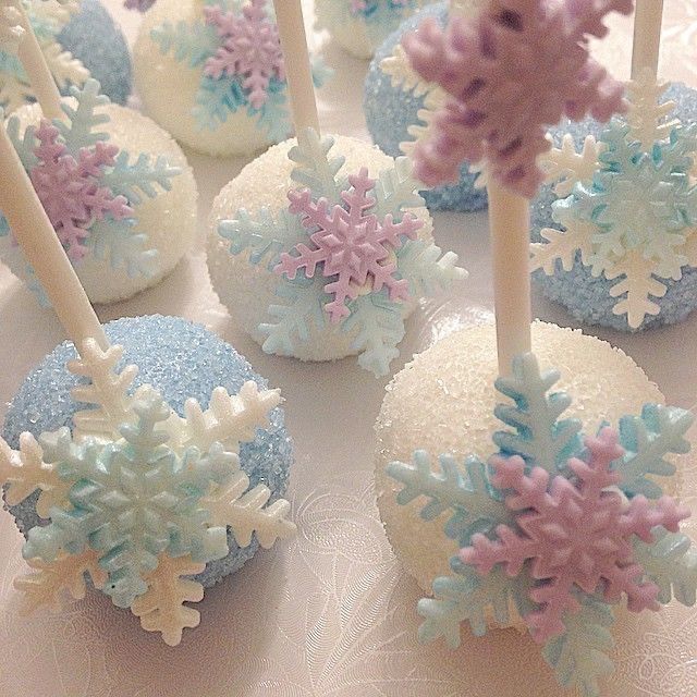 snowflake cake pops are arranged on a white tablecloth with pink and blue frosting