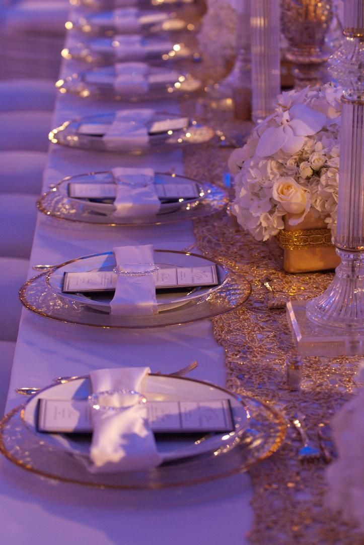 the table is set with silver plates and white napkins, gold rimmed centerpieces