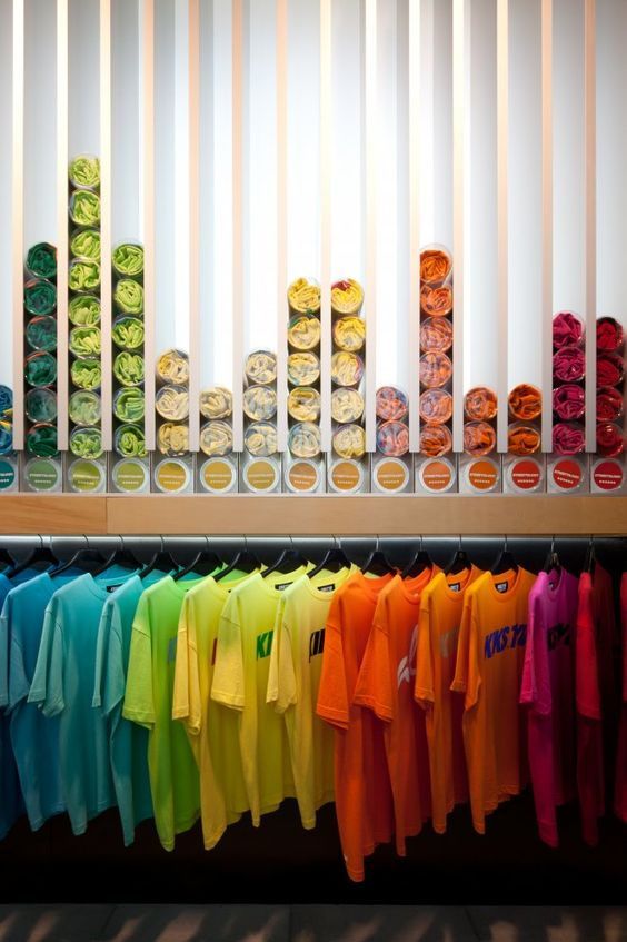 colorful shirts are hanging on the rack in front of a window with white vertical blinds