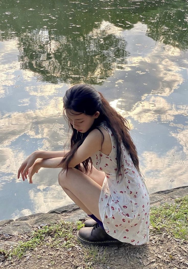 a young woman sitting on the ground next to a body of water