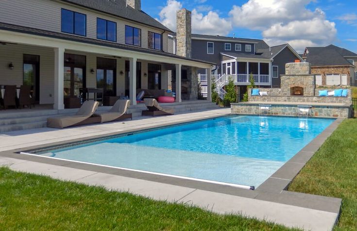 a large swimming pool in the middle of a lawn with lounge chairs and an open patio area