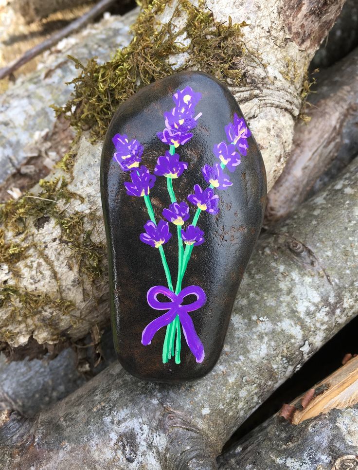 a rock with purple flowers painted on it and a bow tied around the top is sitting on a tree branch