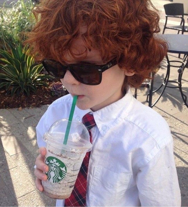 a young boy with red curly hair wearing sunglasses and holding a starbucks drink in his hand