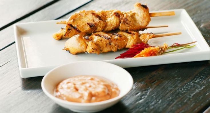 chicken skewers and dipping sauce on a white plate