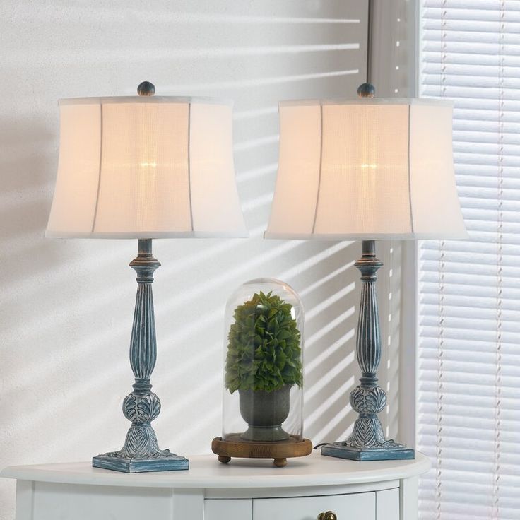 two lamps sitting on top of a white table next to a potted plant in a vase