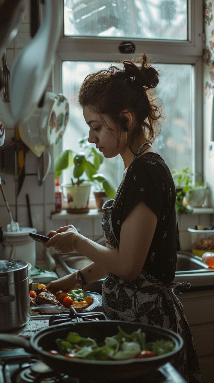 a woman standing in a kitchen preparing food on top of a stove next to a window