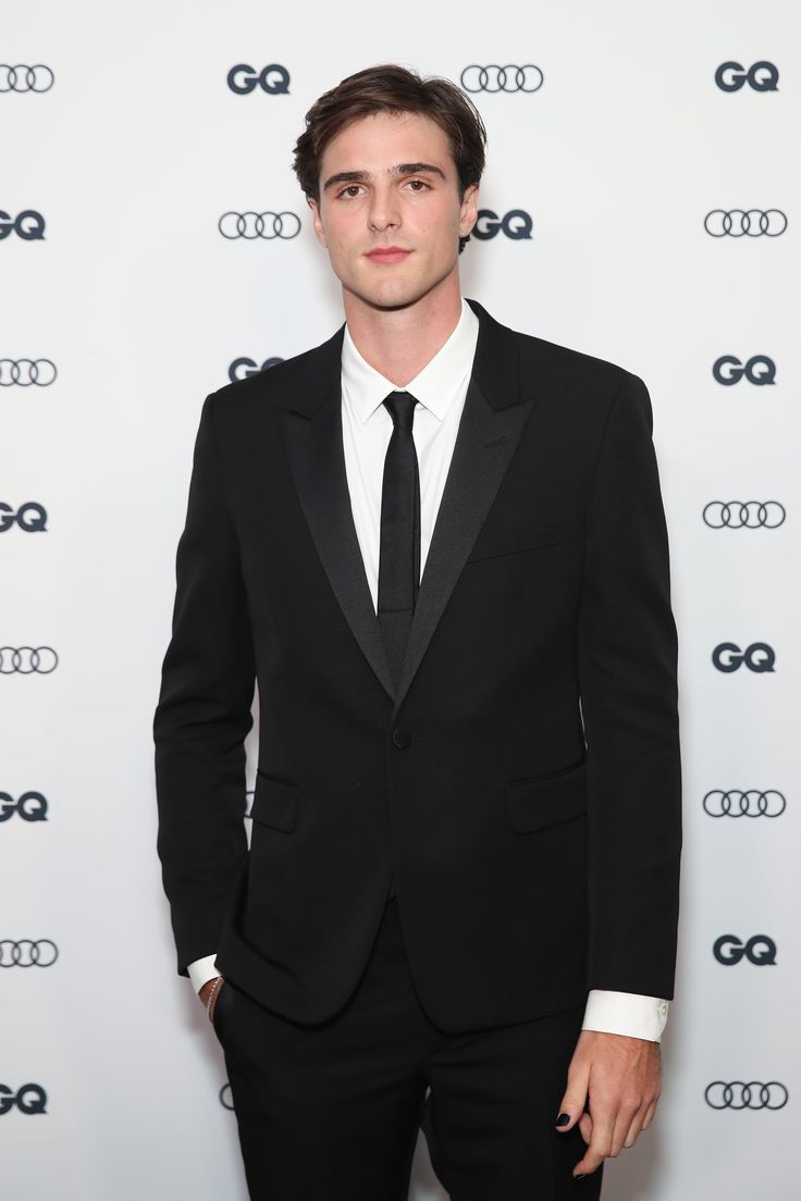 a man in a suit and tie standing on a red carpet with an audi logo behind him