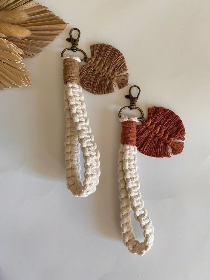 two tasseled keychains hanging from hooks on a white surface next to a gold leaf