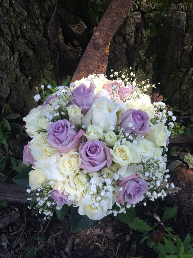 a bouquet of white and purple flowers sitting on top of a wooden bench next to a tree