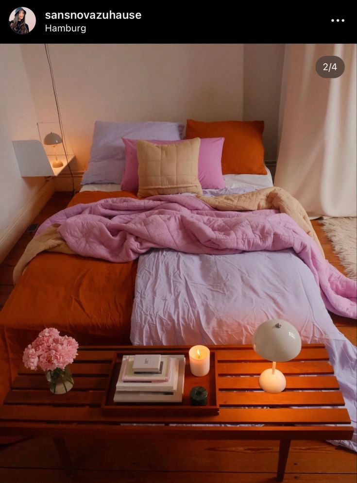 a bed with pink and orange sheets on top of it next to a night stand