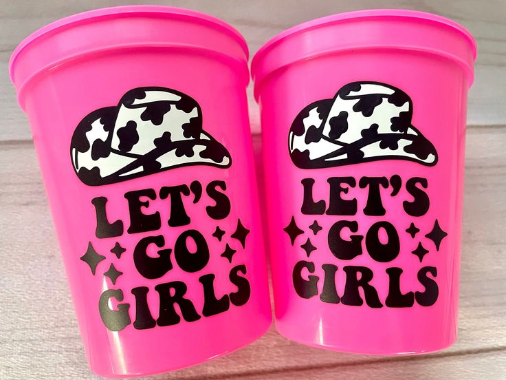 two pink plastic cups with black and white designs on the lids that say let's go girls