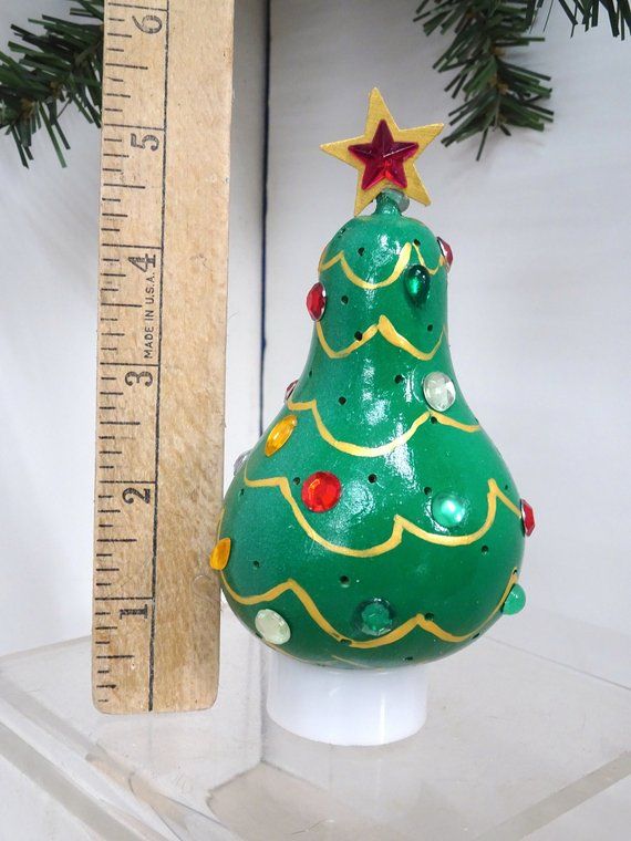 a green christmas tree ornament sitting on top of a white shelf next to a ruler