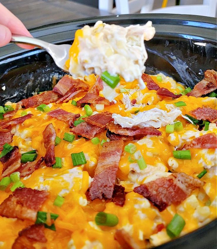 a person scooping some food out of a crock pot with bacon and green onions