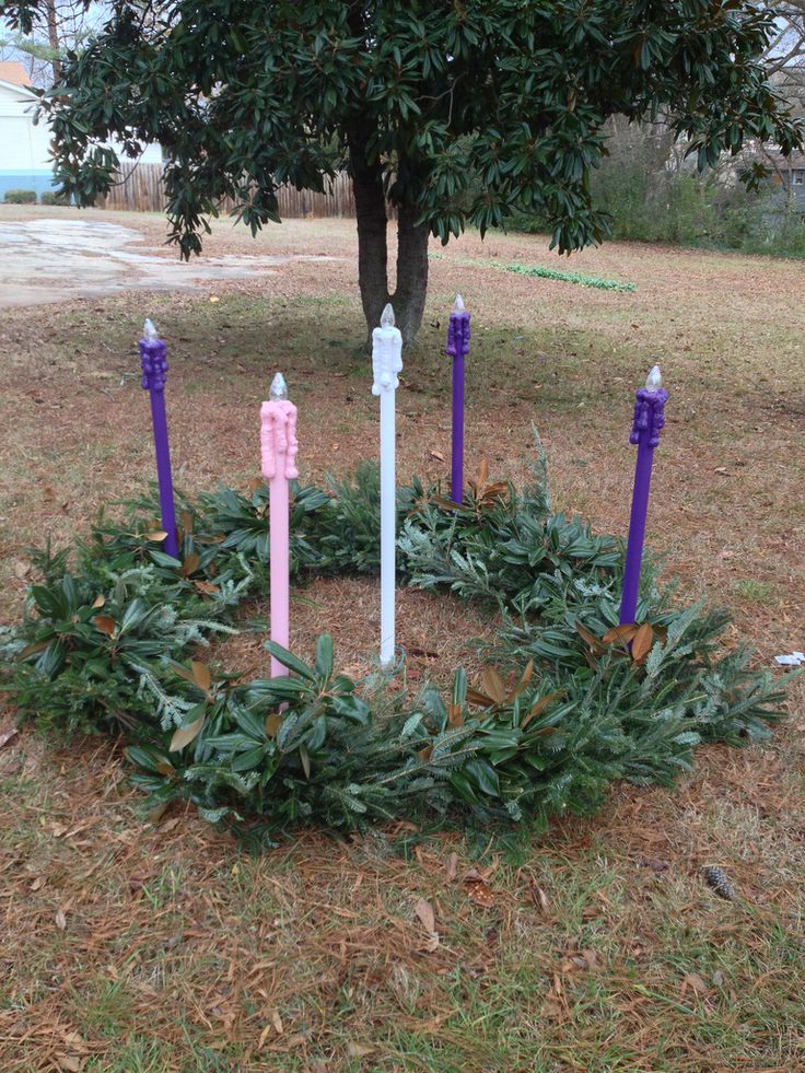 purple and white candles are arranged in a wreath on the ground near a green tree