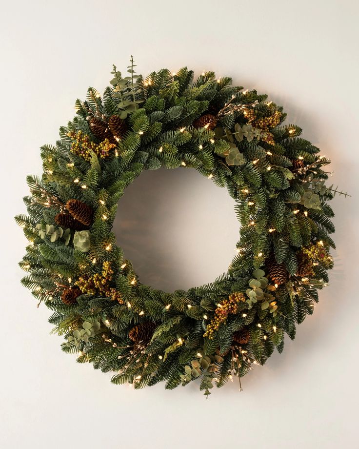 a christmas wreath with pine cones and lights on the front is hung on a wall