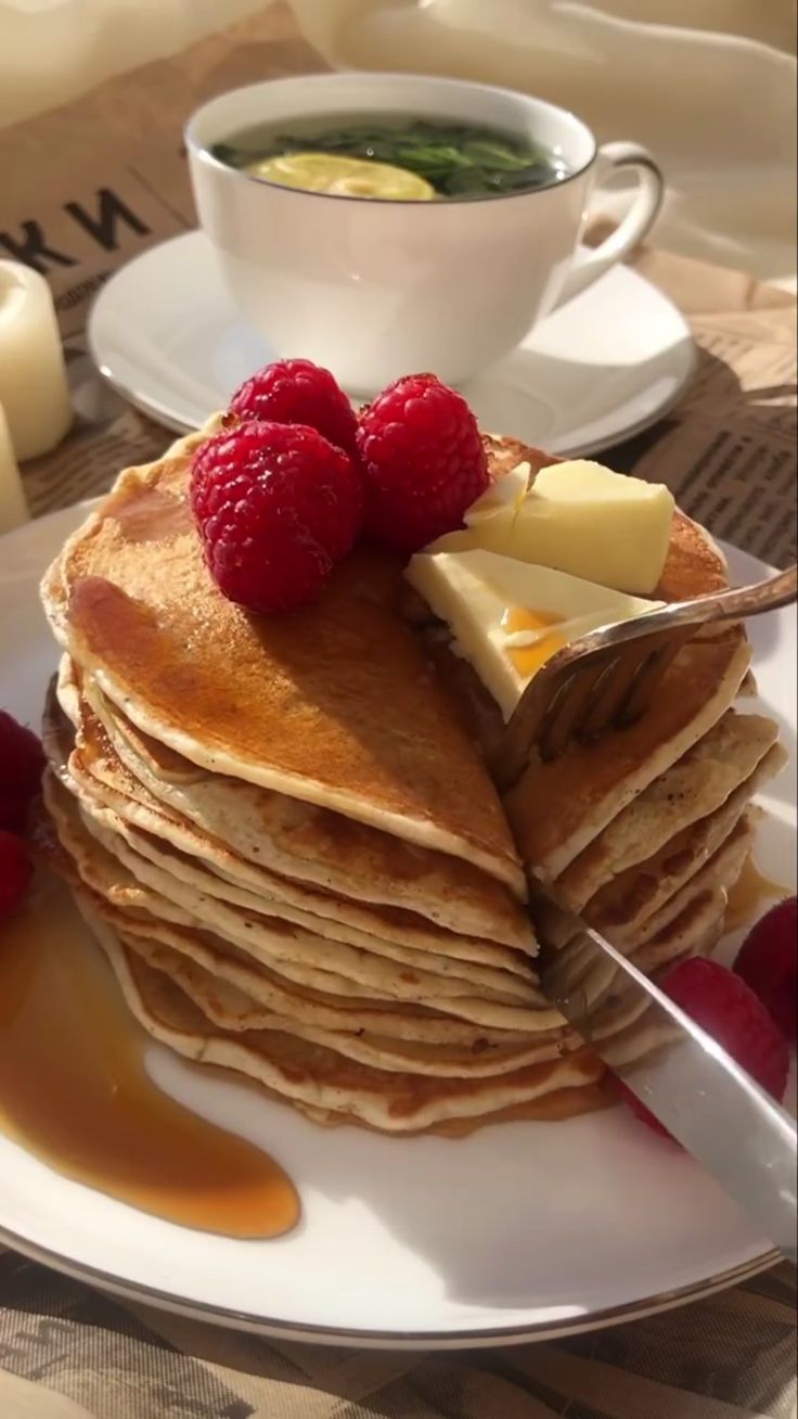 a stack of pancakes on a plate with butter and raspberries next to syrup