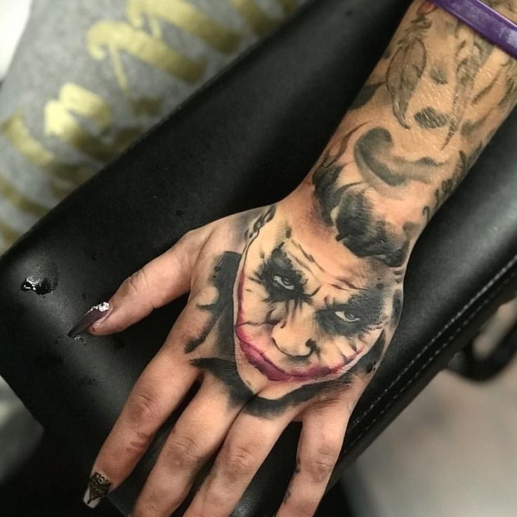 a person with a tattoo on their hand holding a black suitcase and wearing a joker mask