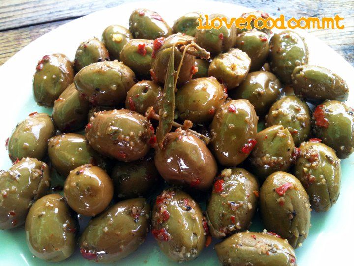 some green olives on a white plate with red pepper sprinkled on them