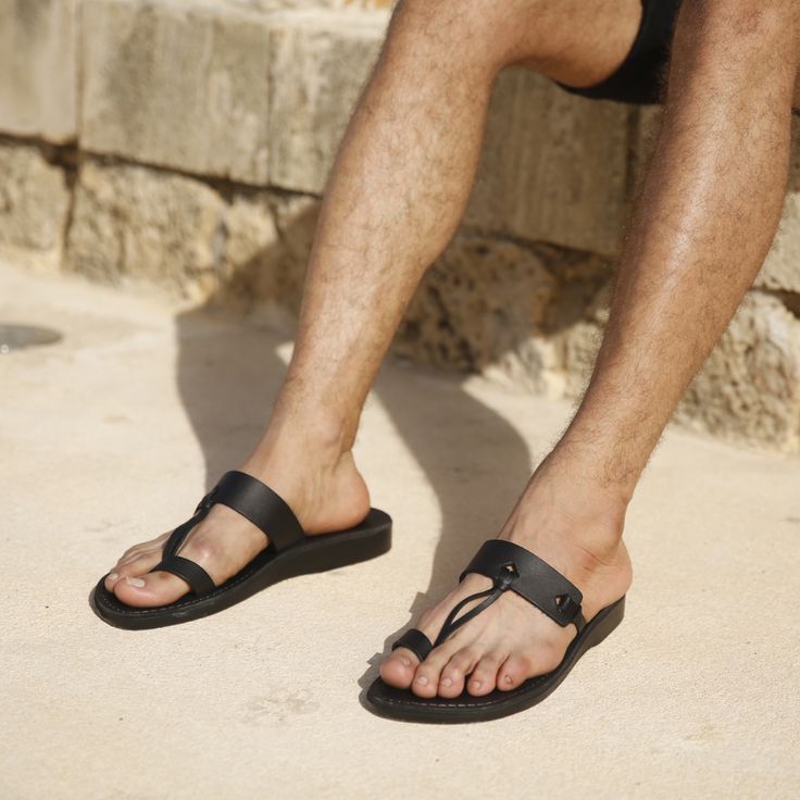 The David men's toe loop sandal is a contemporary take on minimalism. Slip your feet into this open-back flip flop with its sleek silhouette and free yourself from life's complexities. Sturdy arch strap and toe loop provide support. Vegetable tanned leather upper sole shapes to your foot with each step. Water-resistant sandals soften and acquire patina over time, perfect for office strides. Our master Artisans create each Jerusalem Sandal with a customized touch, providing unparalleled quality n Modern Black Toe Loop Sandals, Black Toe Ring Sandals With Leather Footbed, Modern Slides With Single Toe Strap For Beach, Modern Beach Slides With Single Toe Strap, Modern Black Toe Post Sandals, Modern Toe Loop Sandals For Beach, Modern Toe Ring Sandals For Beach, Modern Adjustable Open Toe Flip Flops, Black Leather Footbed Toe Loop Flip Flops